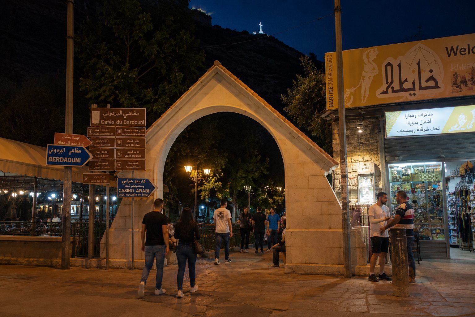Entrance archway to the Berdawni promenade in Zahlé at night, with cafés and shops